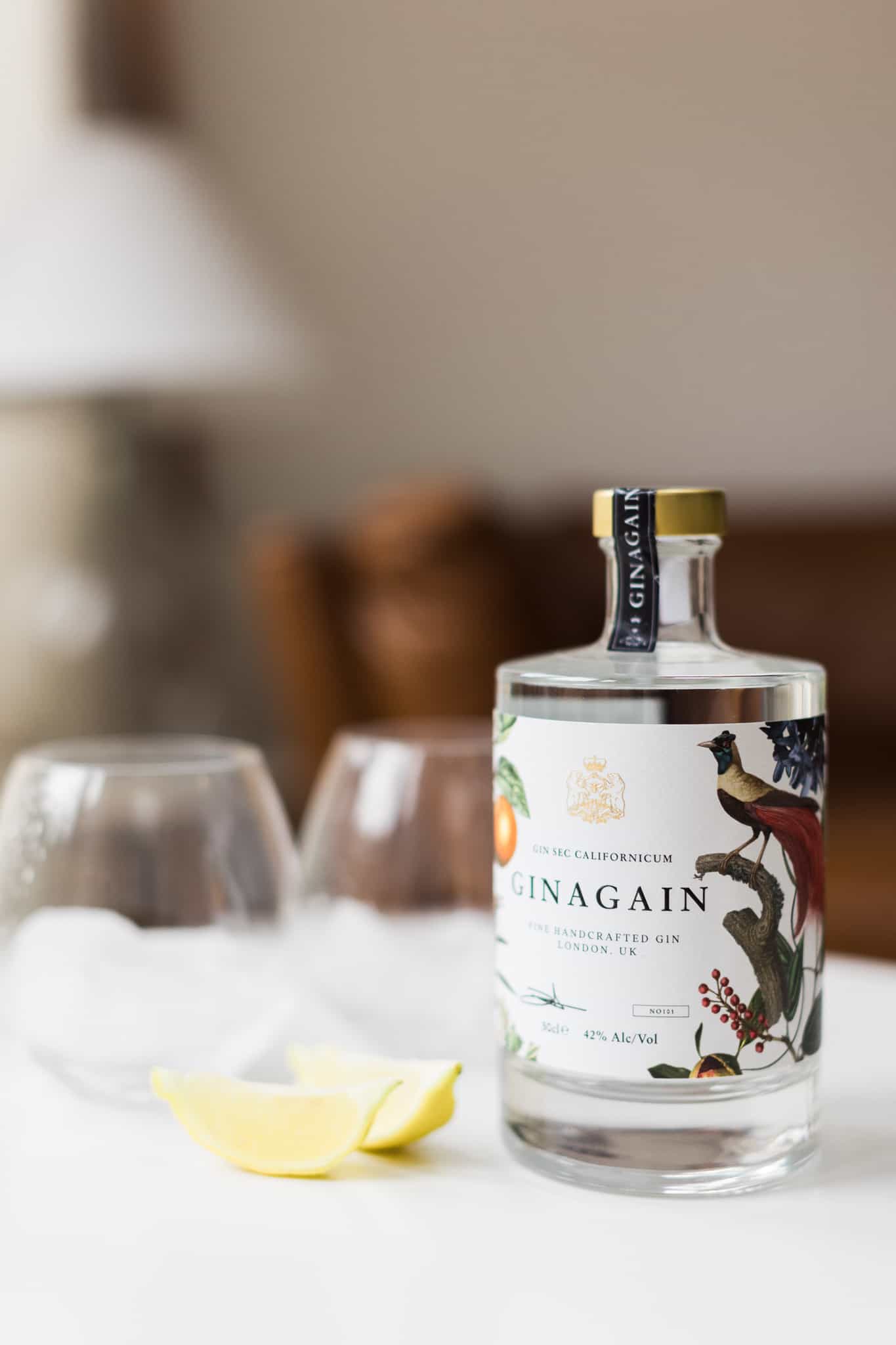 A bottle of Ginagain gin sits on a white table with two glasses and a slice of lemon