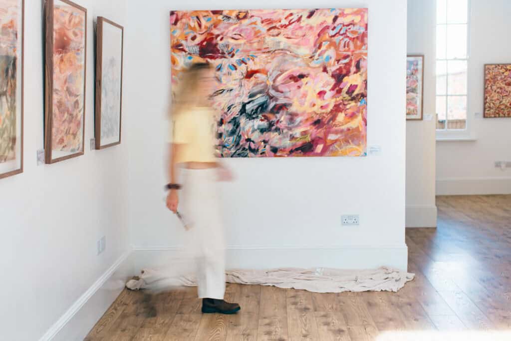 Artist Emma Howell walks past one of her paintings on the wall, blurred by motion blur.