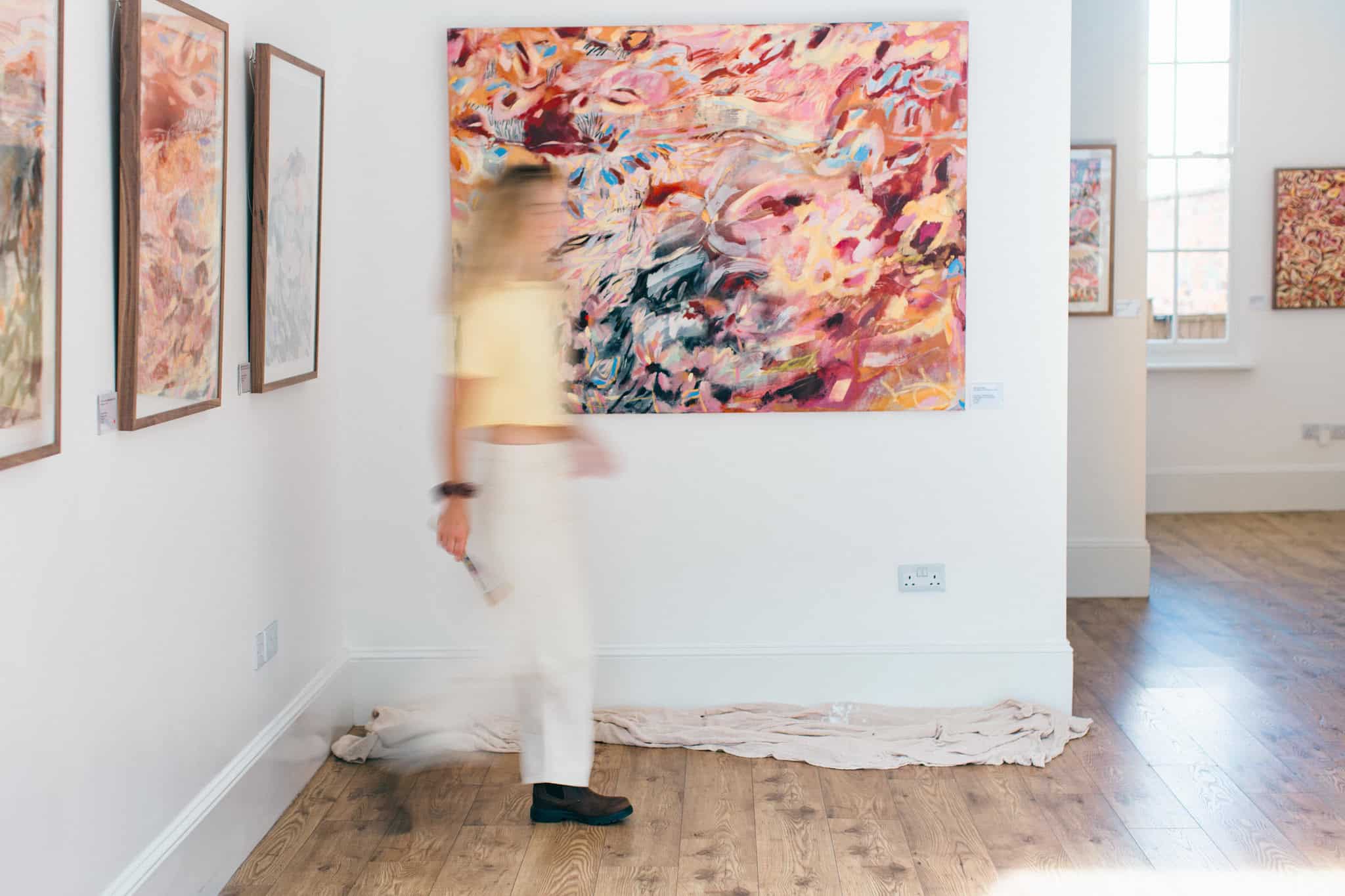 Artist Emma Howell walks past one of her paintings on the wall, blurred by motion blur.