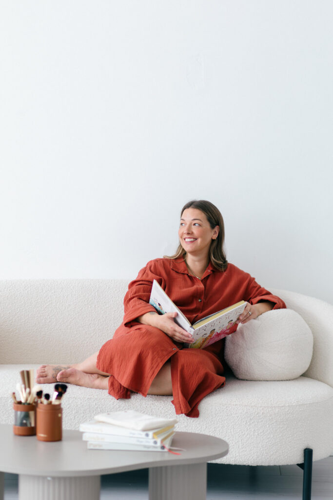 Cotswold stylist Kerry Pargeter-Smith wears a rust coloured dress and smiles sitting on a cream sofa.