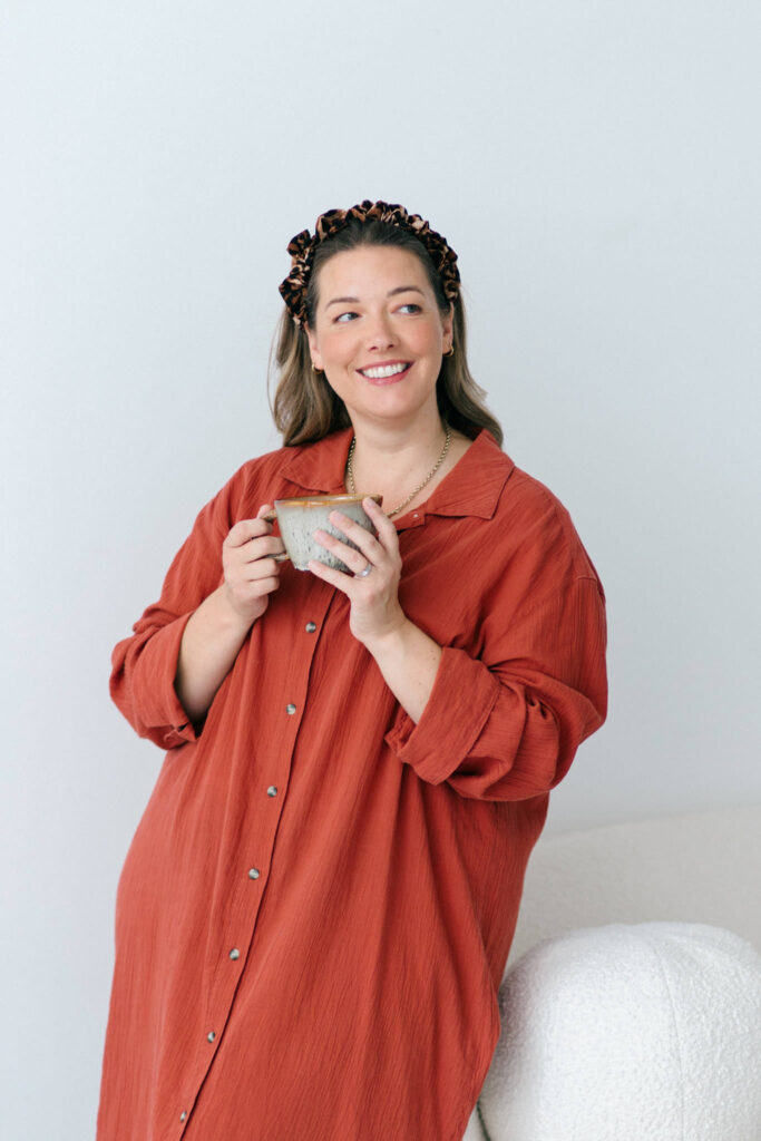 Gloucestershire stylist and make up artist Kerry Pargeter-Smith on a cream sofa in a rust coloured shirt dress.