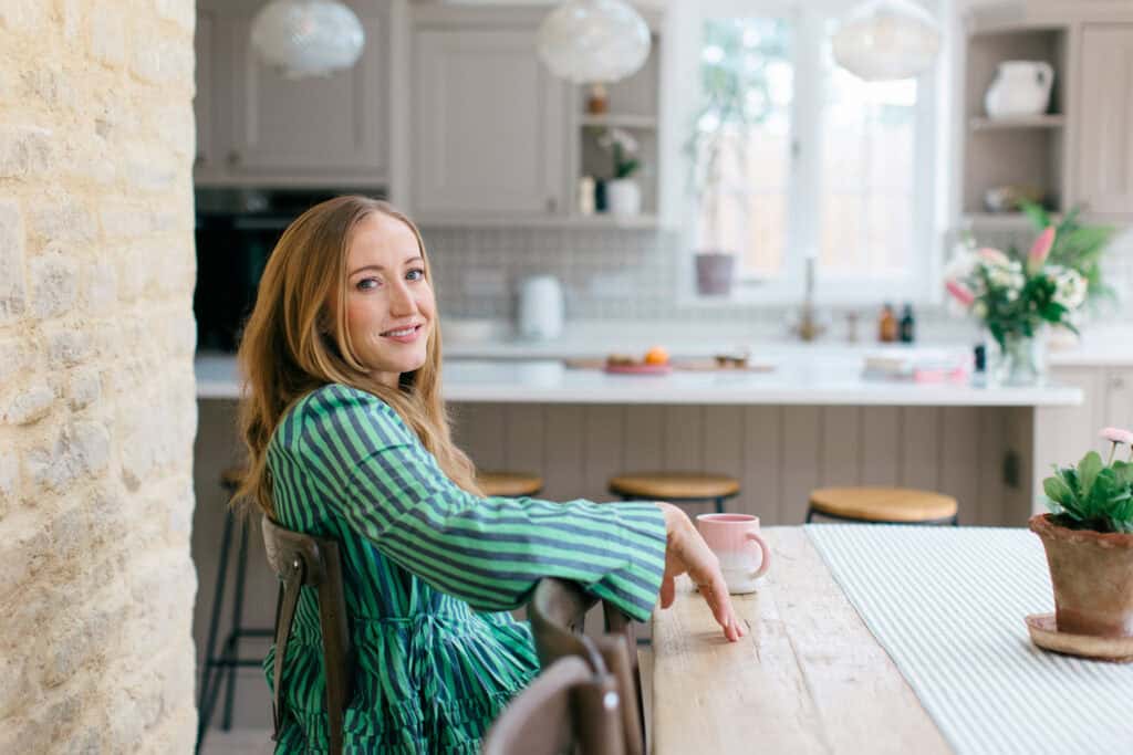 Children's Dietitian Lucy Upton dressed in green sits in a beautiful airy Cotswold kitchen