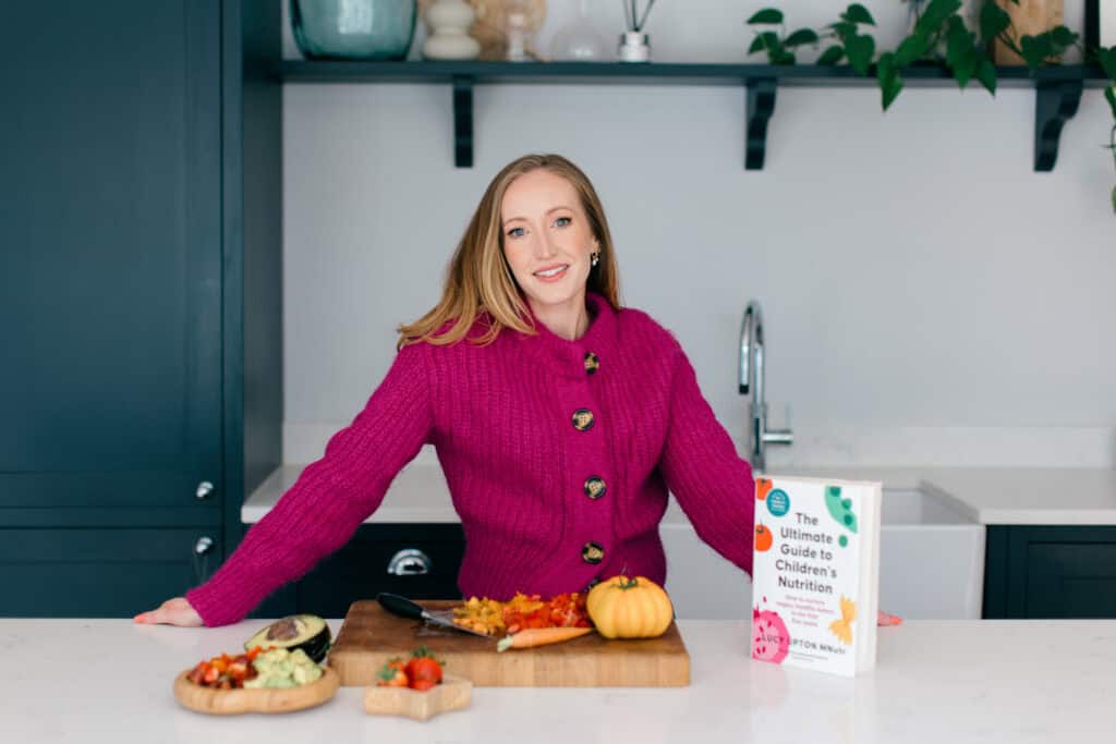Children's Dietitian and author Lucy Upton smiles at a kitchen island with her new book in front of her.